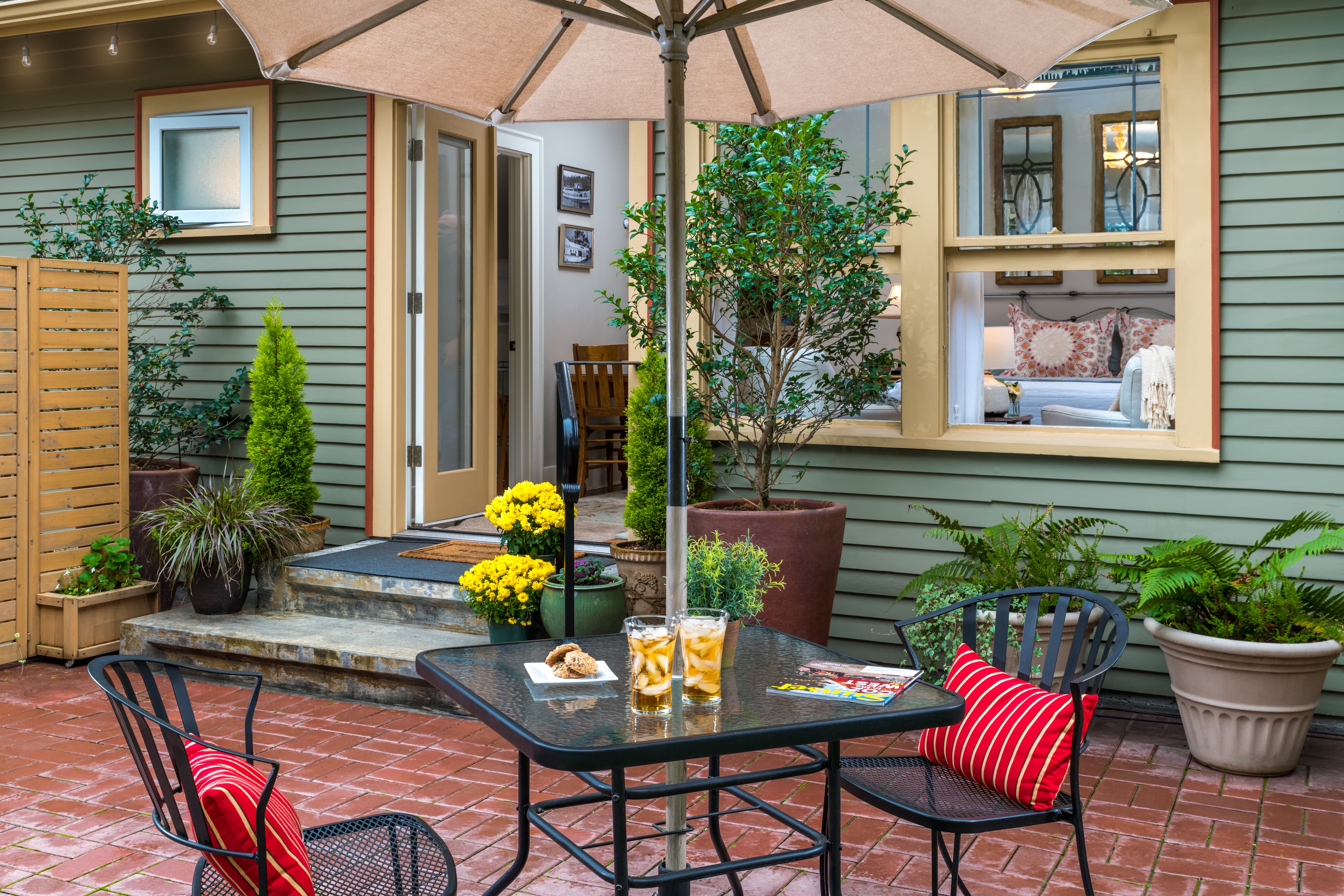 Cozy patio area with table, chairs, umbrella, and refreshments outside an open door to a house.