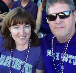 A couple smiles while wearing purple attire and beads at an outdoor event.