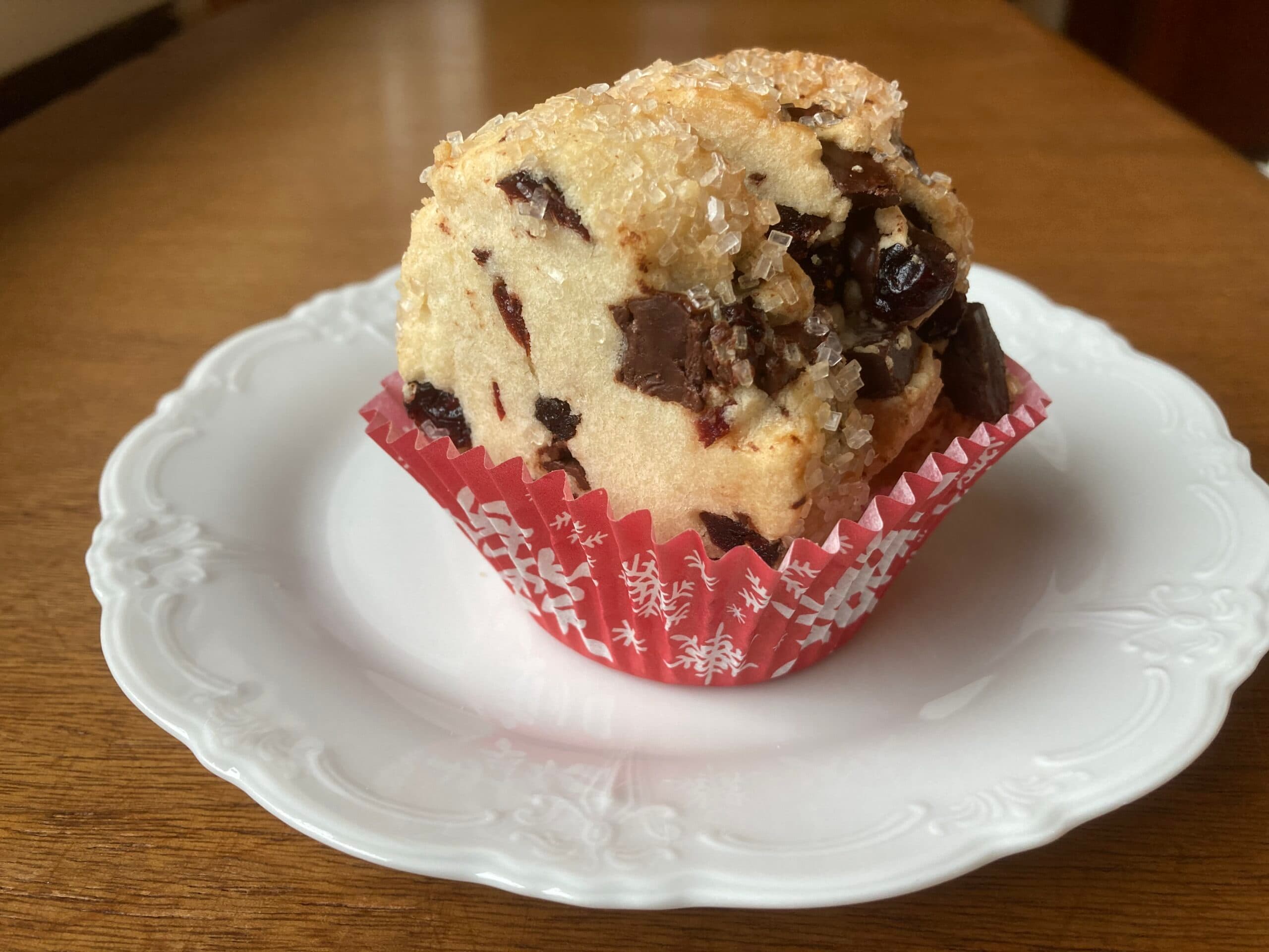 A chocolate chip muffin in a festive red cupcake liner sits on a white plate.