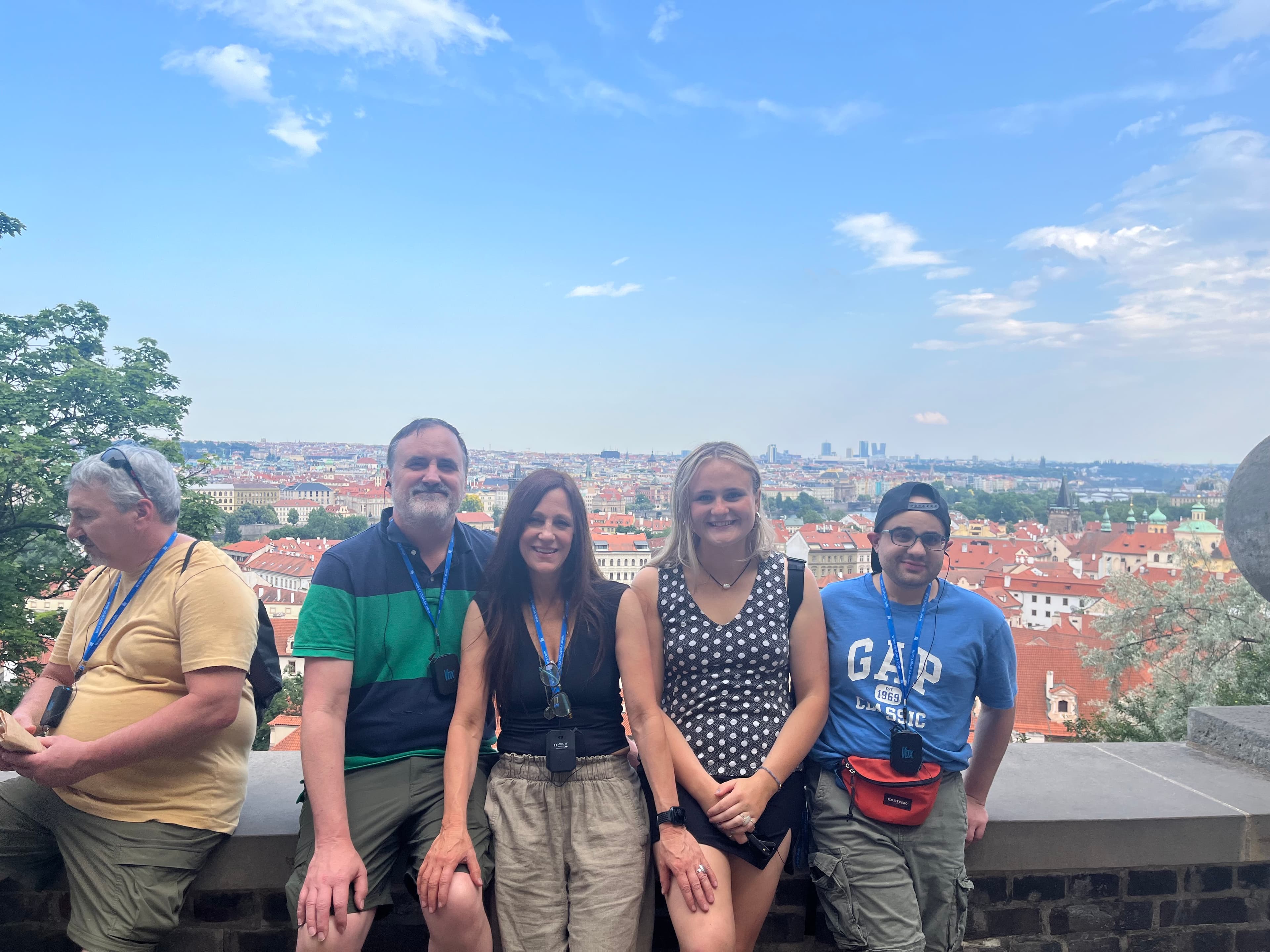 A group of four people stands on a wall overlooking a city skyline under a blue sky. A group of four people stands on a wall overlooking a city skyline under a blue sky.