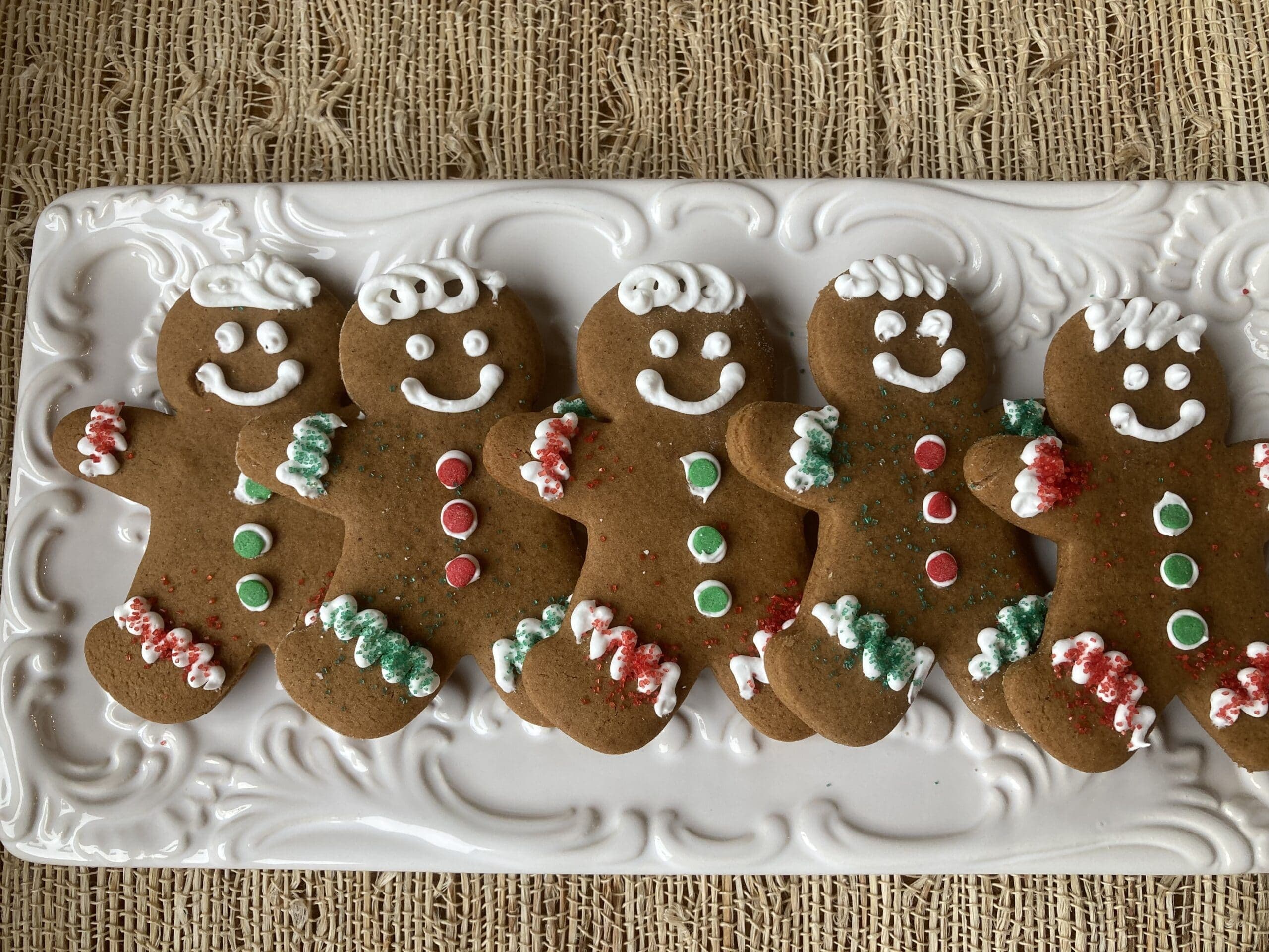 A plate of decorated gingerbread cookies shaped like smiling gingerbread men, with icing and candy accents.
