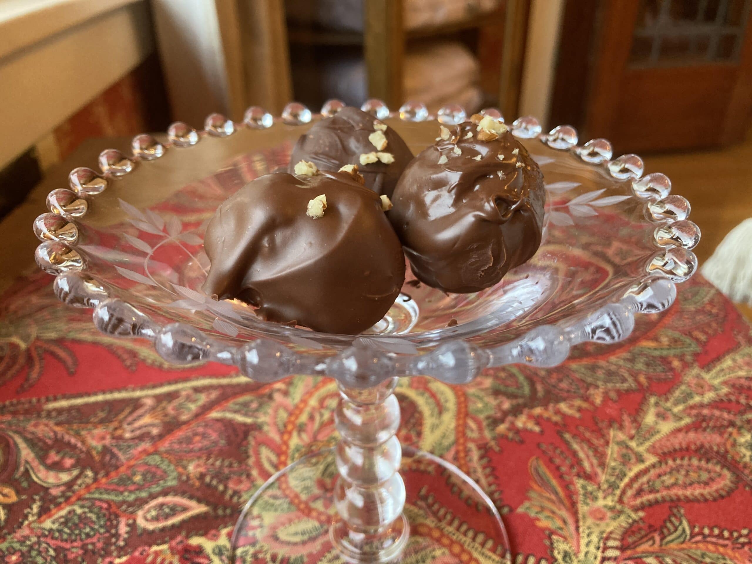 A glass dish holds three chocolate truffles garnished with small pieces of gold leaf.