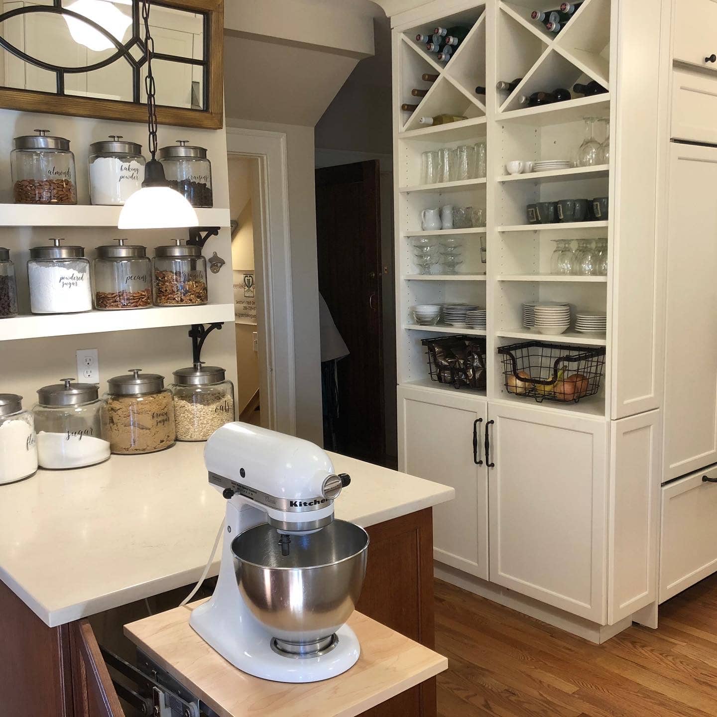 A tidy kitchen featuring a countertop stand mixer, organized glassware, and storage jars.