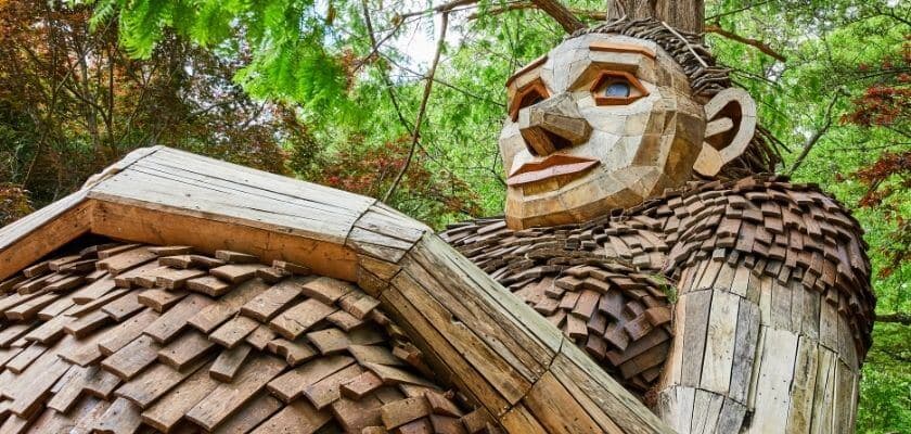 A large wooden sculpture of a seated figure surrounded by green trees.