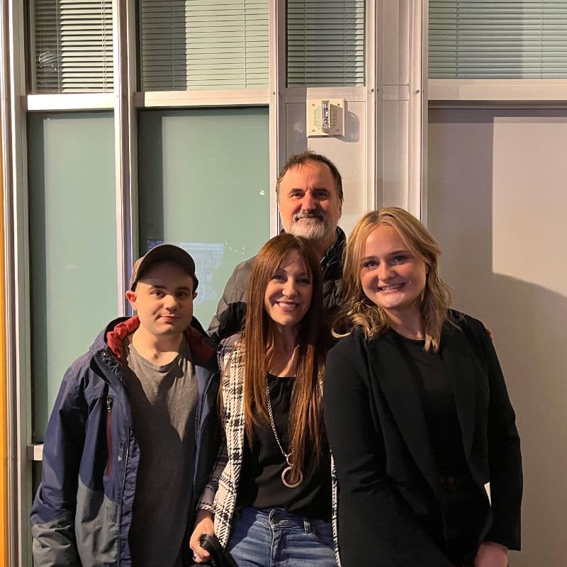 A group of four people poses together for a photo in front of large windows.