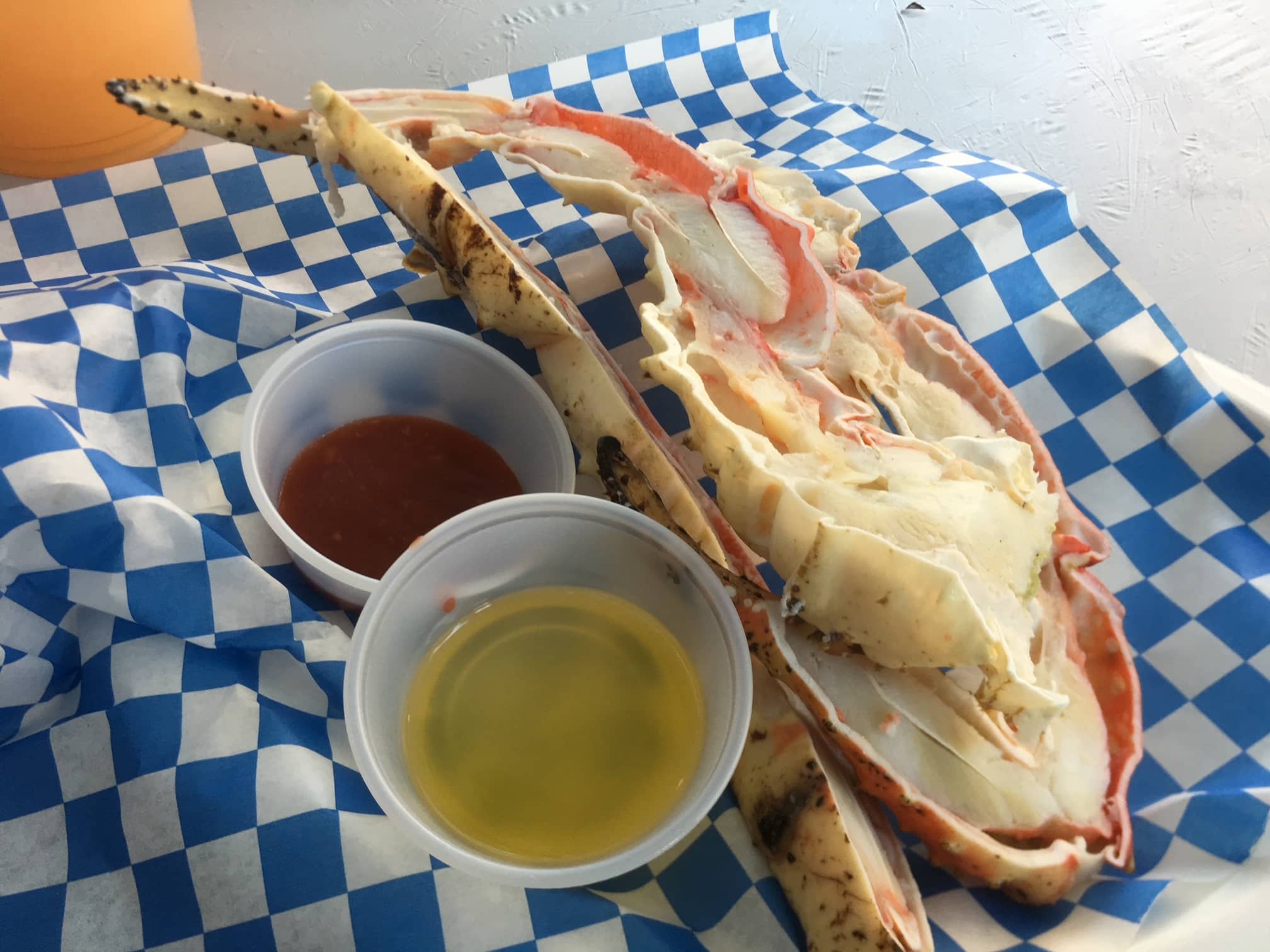 A large crab section served with two dipping sauces on a blue checkered paper.