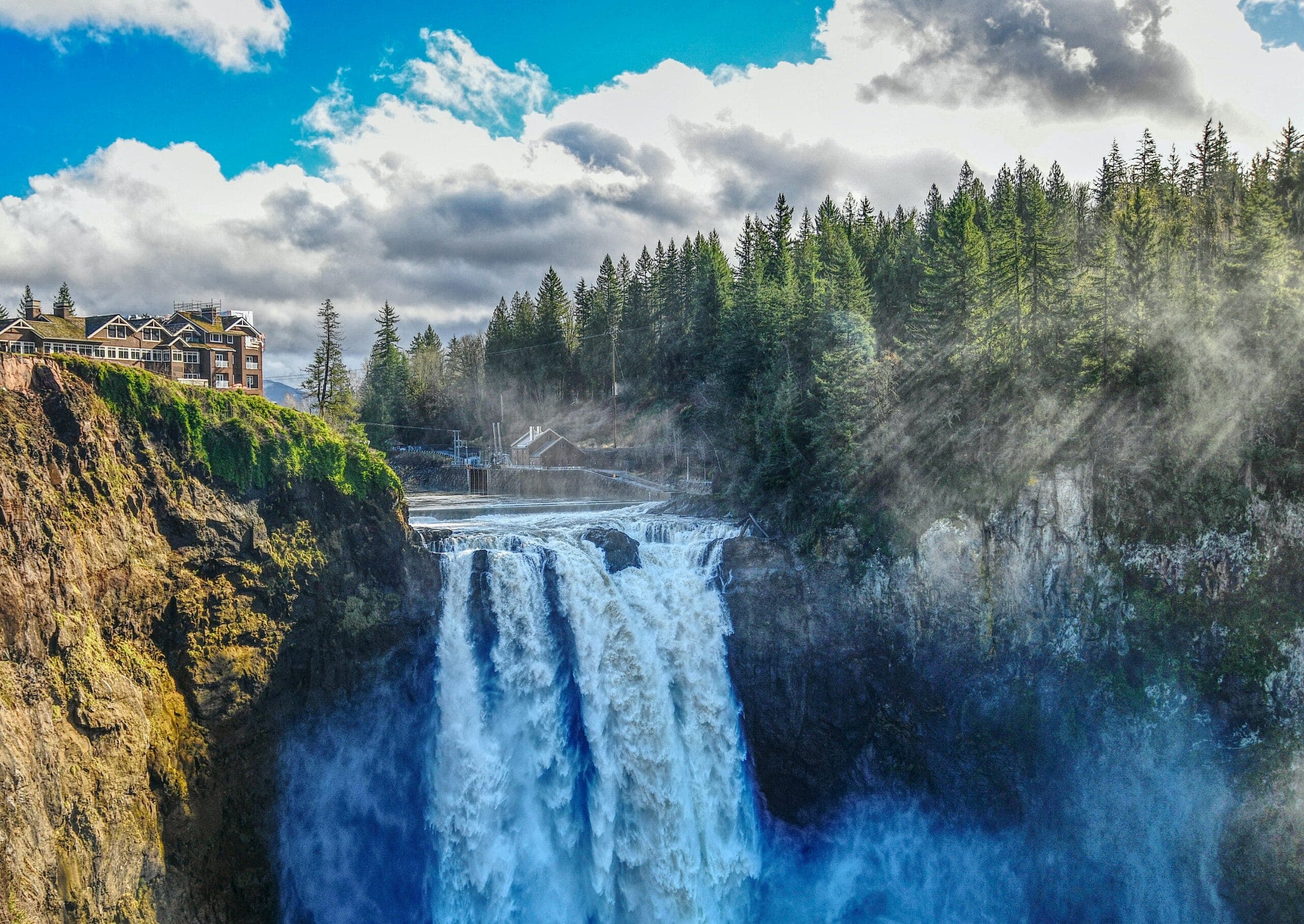 A majestic waterfall cascading down rocky cliffs, surrounded by lush green trees and a cloudy blue sky. A majestic waterfall cascading down rocky cliffs, surrounded by lush green trees and a cloudy blue sky.