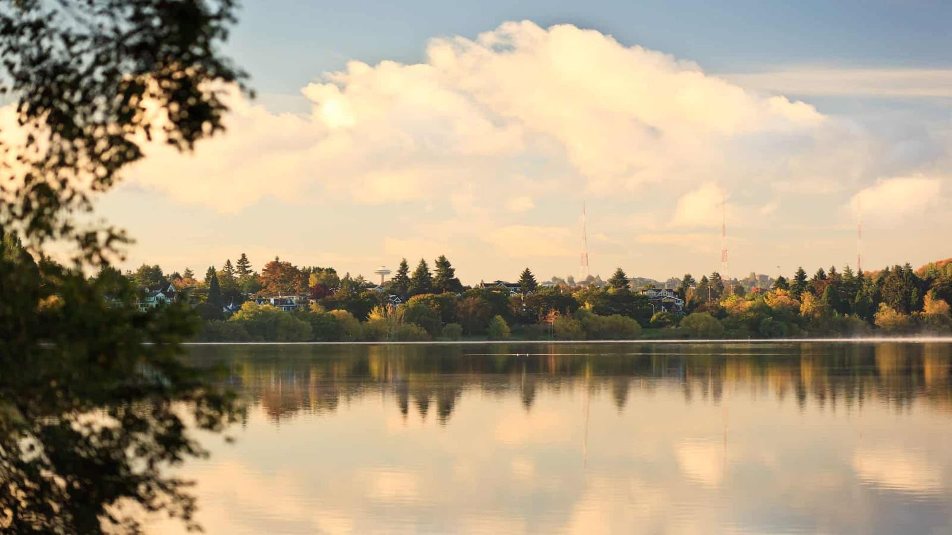 A peaceful lakeside view with reflections of trees and clouds in the water.