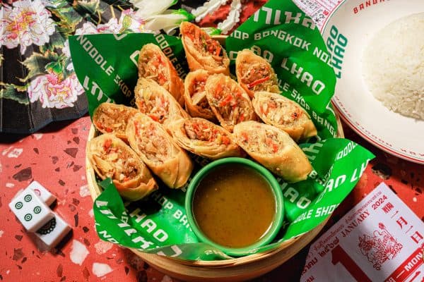 A bamboo steamer basket filled with crispy spring rolls accompanied by a small bowl of dipping sauce. A bamboo steamer basket filled with crispy spring rolls accompanied by a small bowl of dipping sauce.