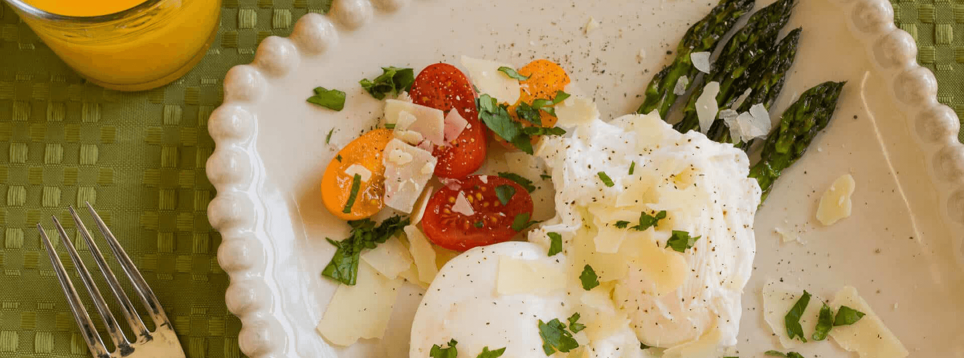A plate of poached eggs, cherry tomatoes, and asparagus garnished with herbs and cheese, alongside a glass of orange juice.