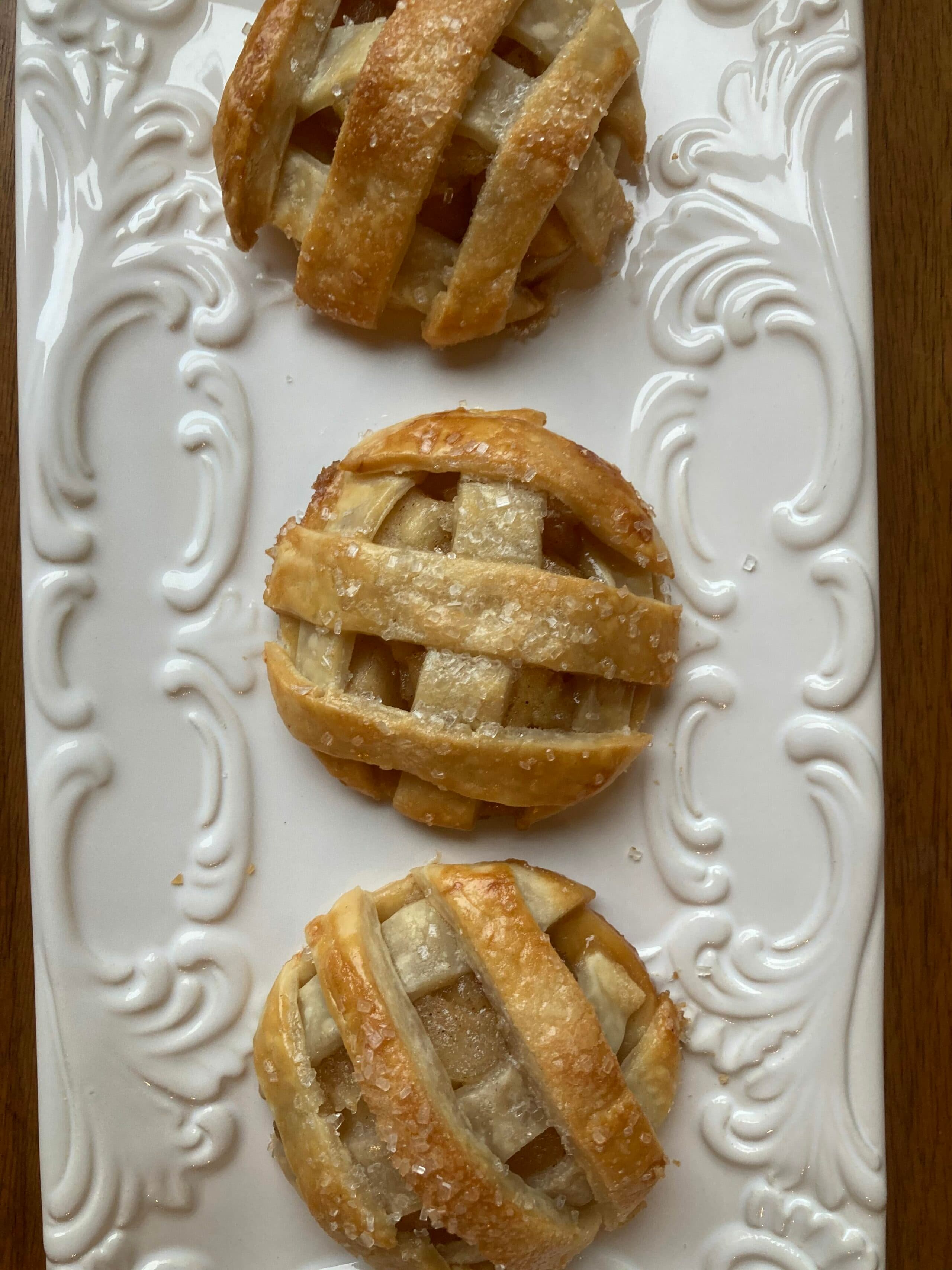 Three lattice-top apple pastries on a decorative white platter.
