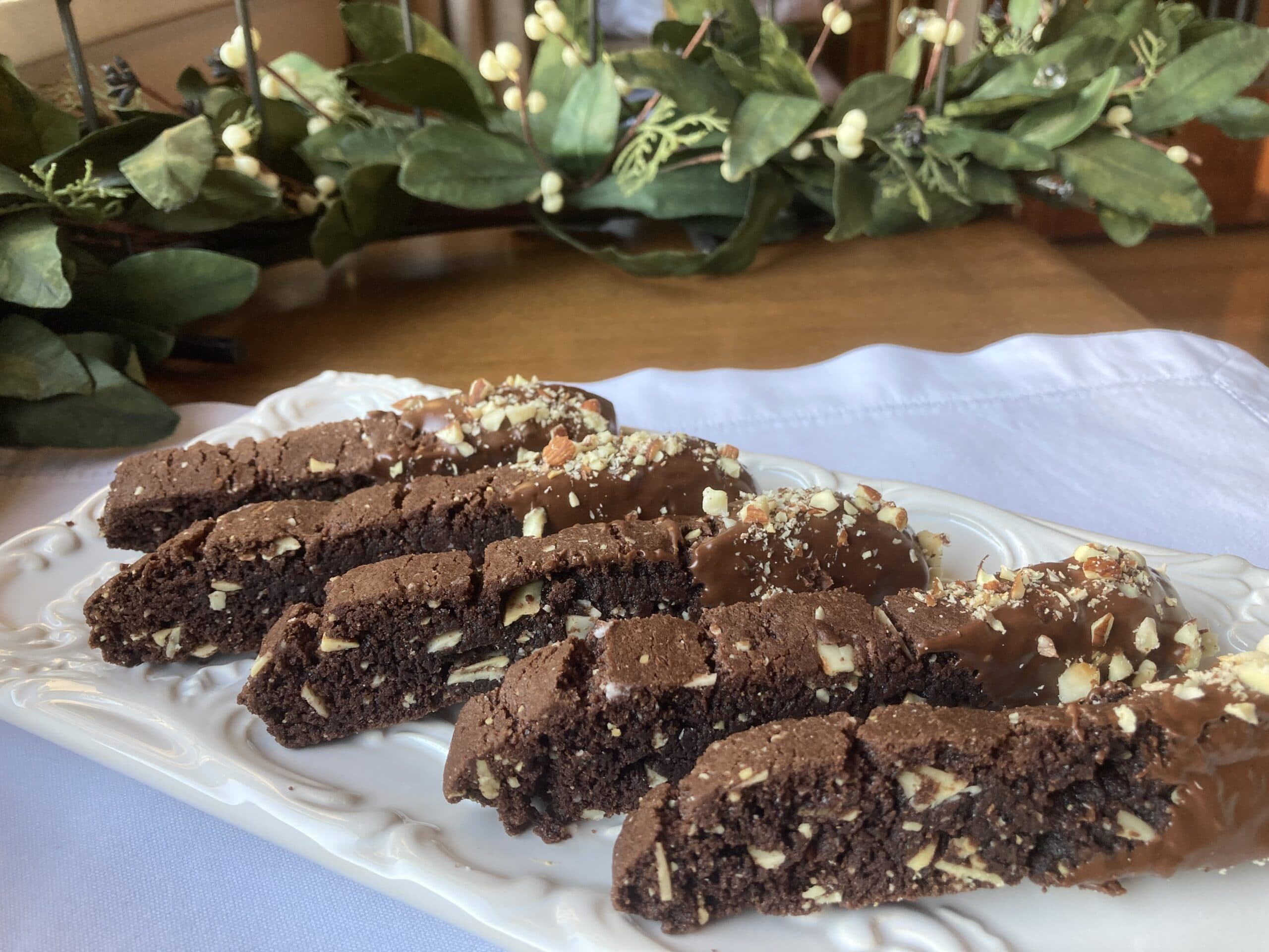A plate of sliced chocolate biscotti topped with nuts and chocolate drizzle.
