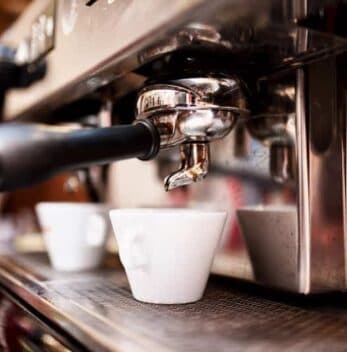 A close-up of an espresso machine pouring coffee into white cups.