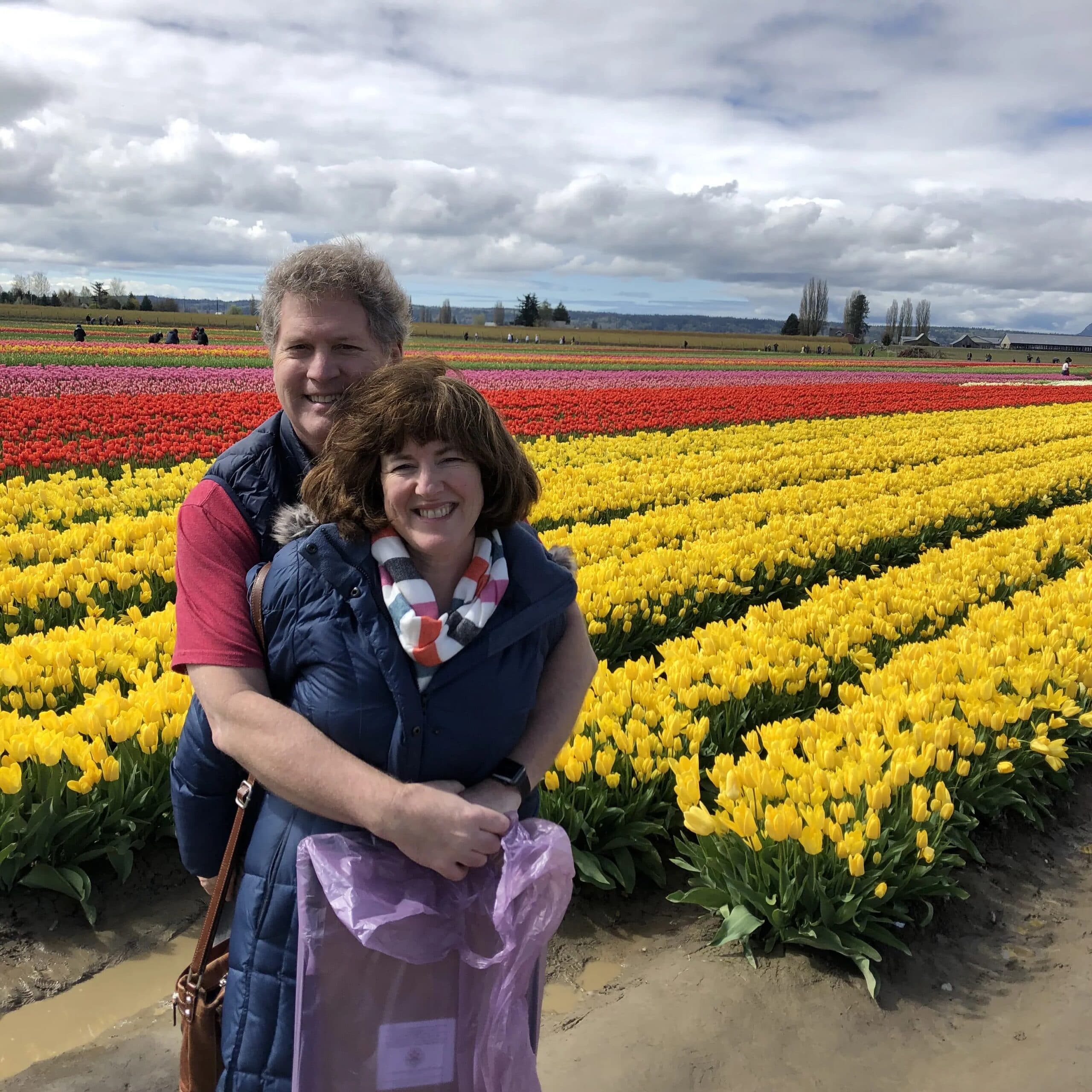A couple smiles together in front of vibrant fields of tulips.
