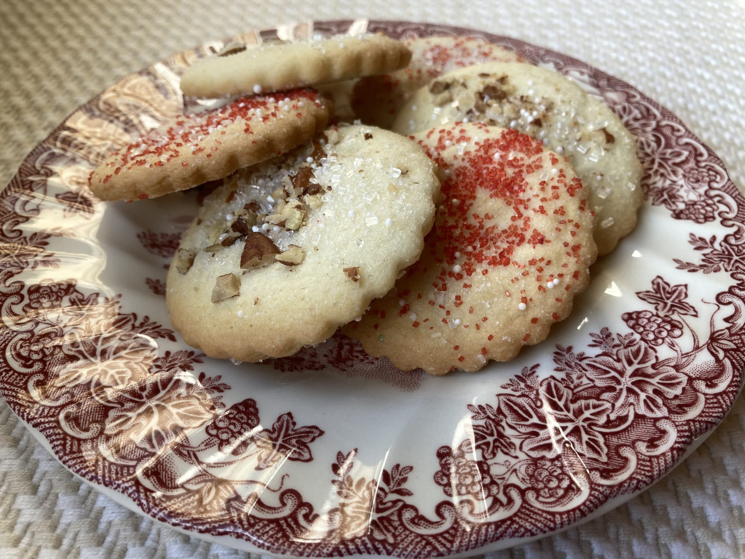 A decorative plate holds several sprinkled cookies with nuts on top.