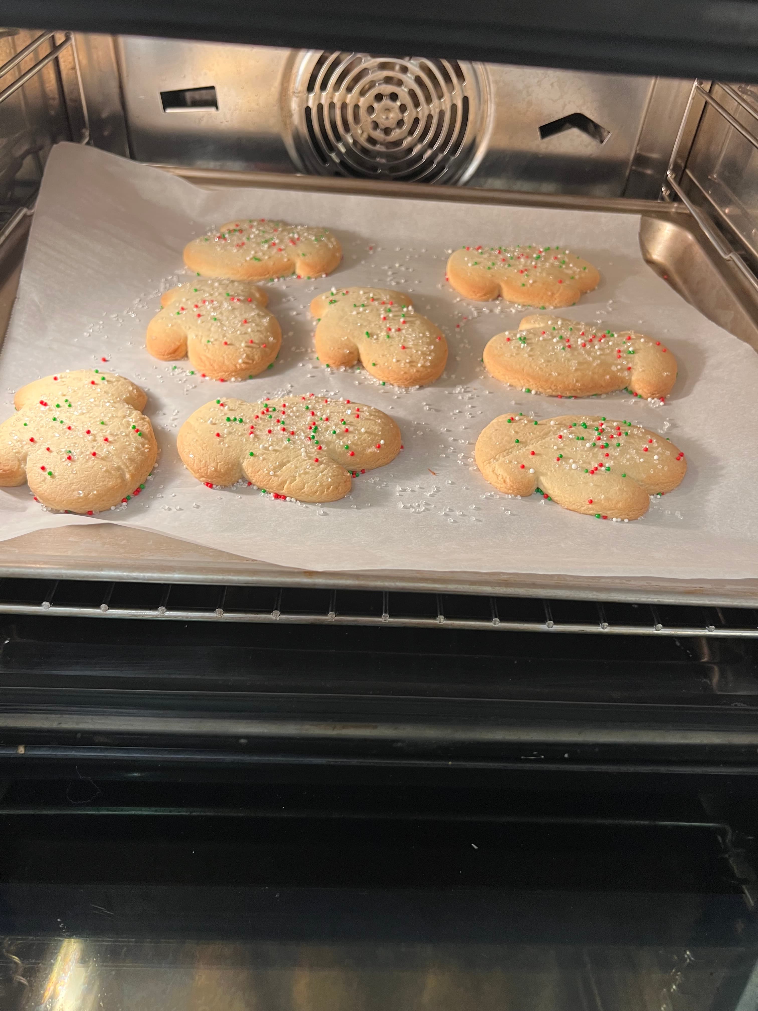 Freshly baked heart-shaped cookies with sprinkles on a baking sheet in the oven.