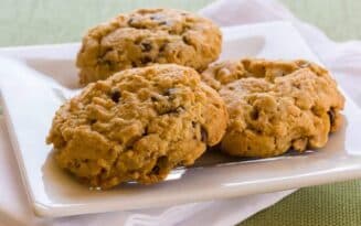 Three oatmeal cookies with chocolate chips on a white plate.