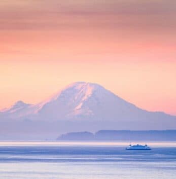 A serene view of a snow-capped mountain at sunset, with a boat sailing in the foreground.
