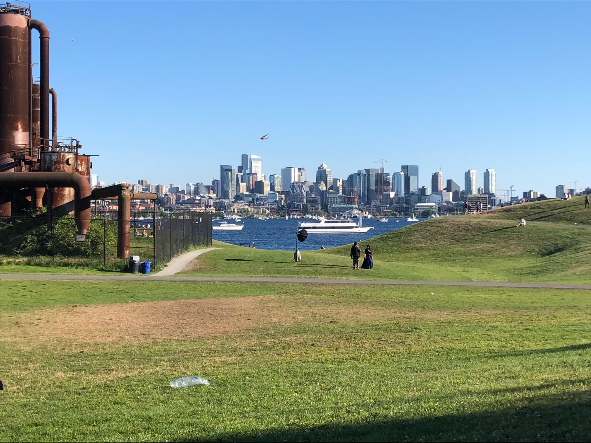 A scenic view of a city skyline across a body of water, with green grass and people walking in the foreground.