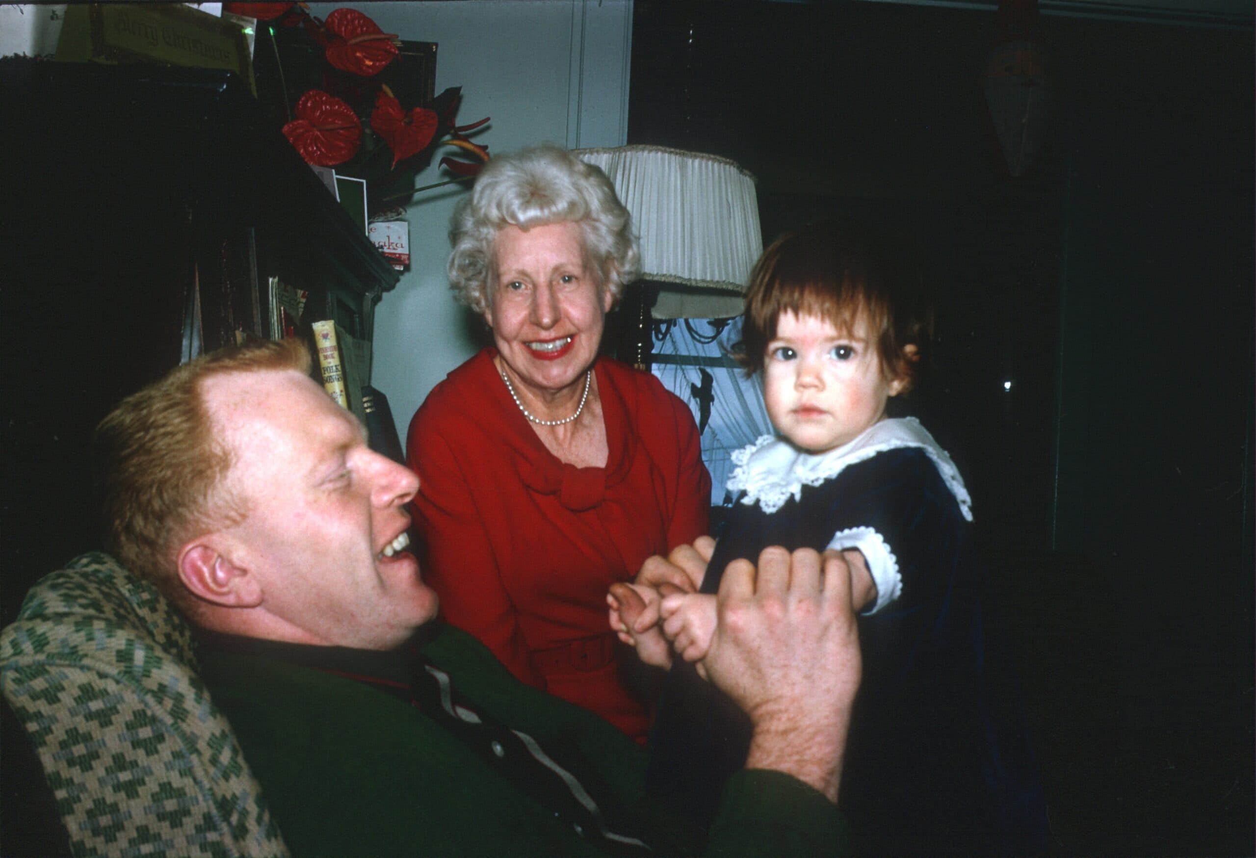 A man and an elderly woman smile at a young girl in a cozy living room setting.