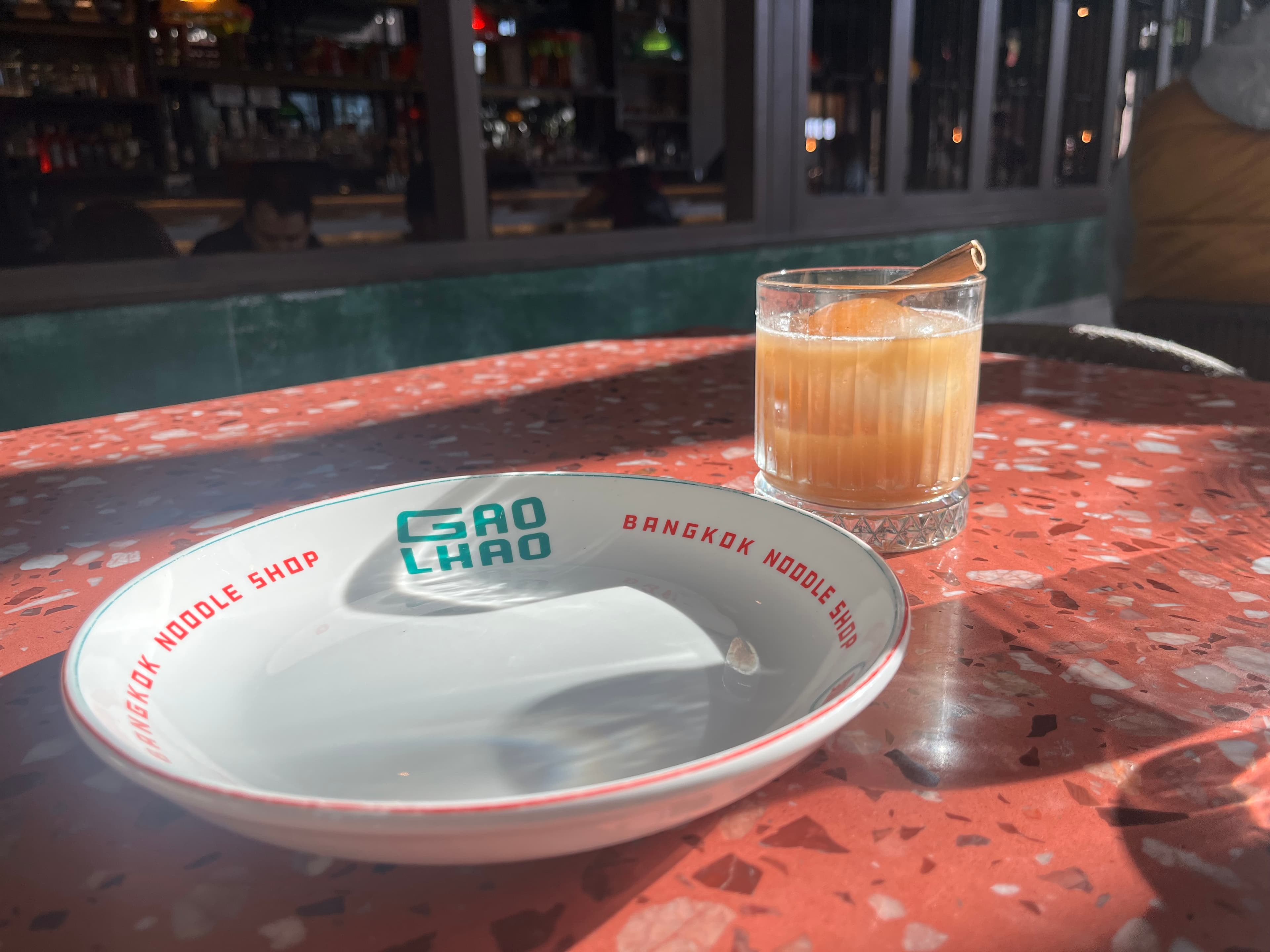 A glass of drink with a cinnamon stick sits next to an empty plate on a colorful table.