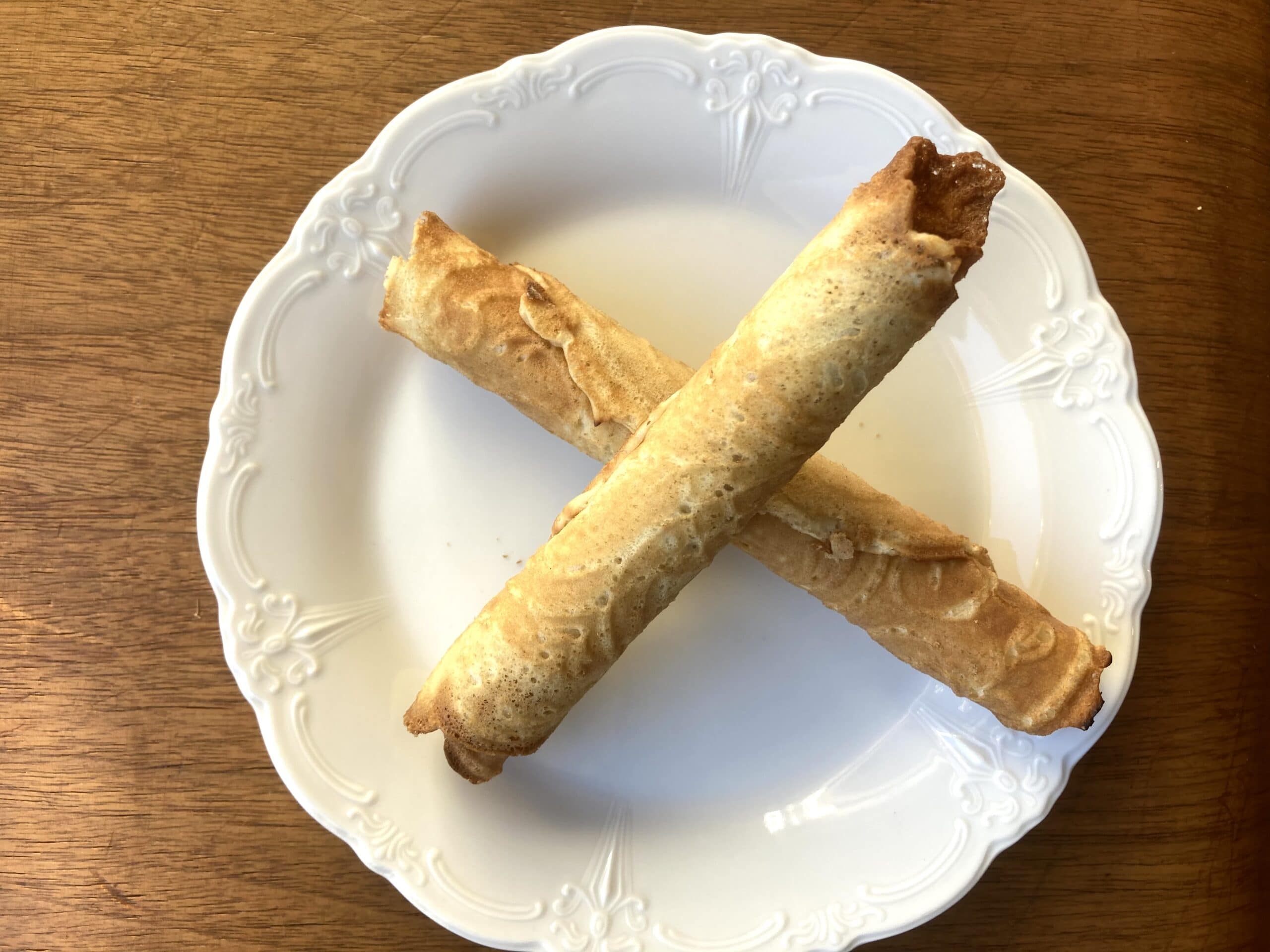 Two rolled pastries arranged in a cross on a white plate.