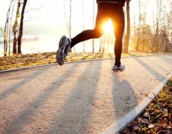 A person jogs on a path surrounded by trees at sunset.