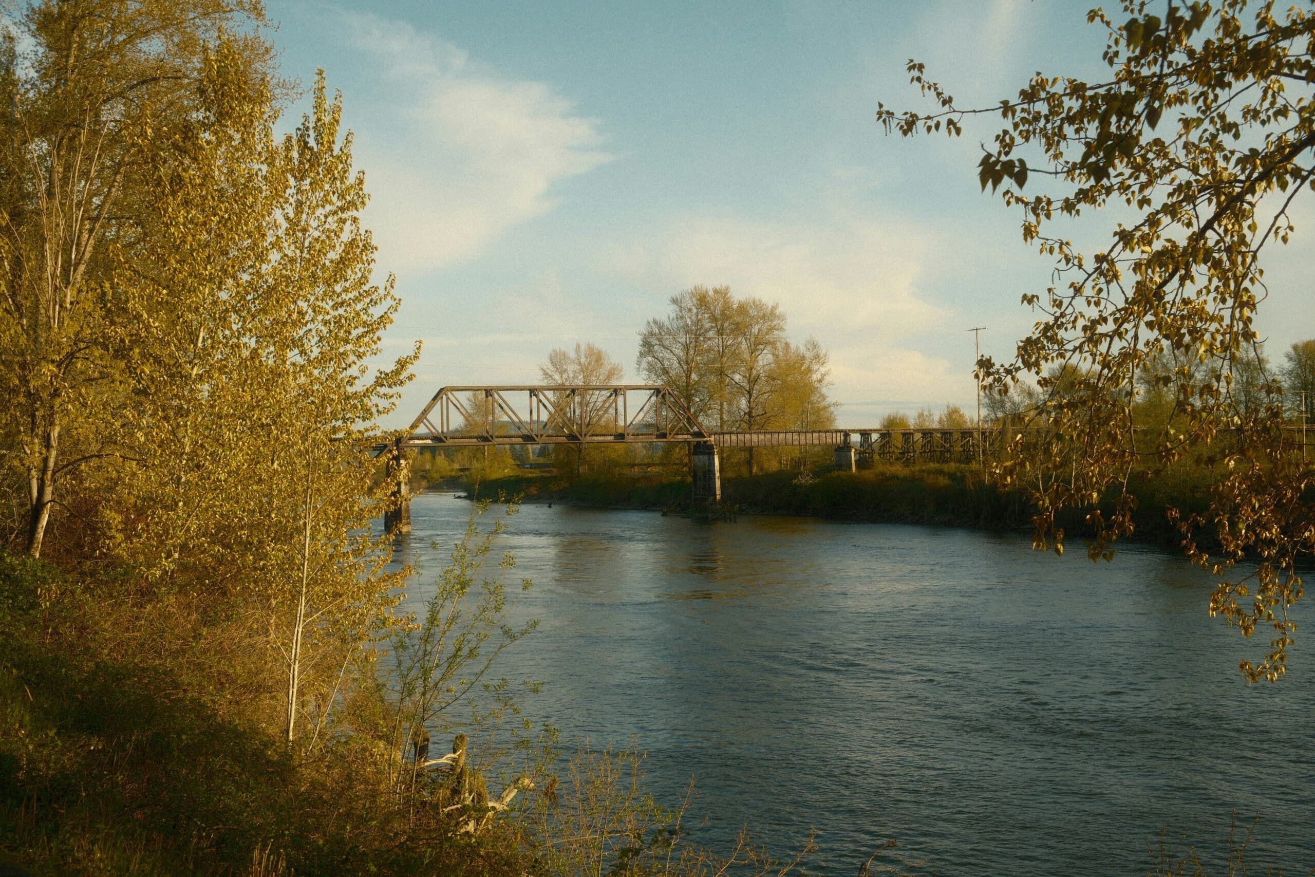 A peaceful river scene with a railroad bridge and autumn foliage. A peaceful river scene with a railroad bridge and autumn foliage.