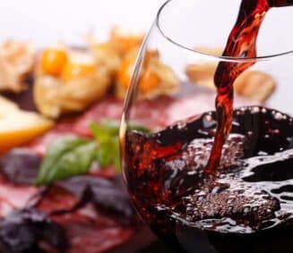 A glass of red wine being poured over a charcuterie platter.