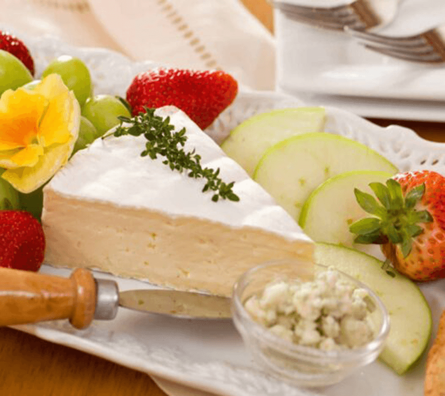 A plate of creamy cheese garnished with fresh herbs, surrounded by strawberries, green grapes, apple slices, and a small bowl of blue cheese.