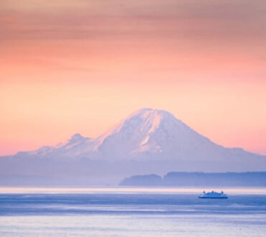 A serene view of a snow-capped mountain against a pastel sky, with a ferry on the calm water below.