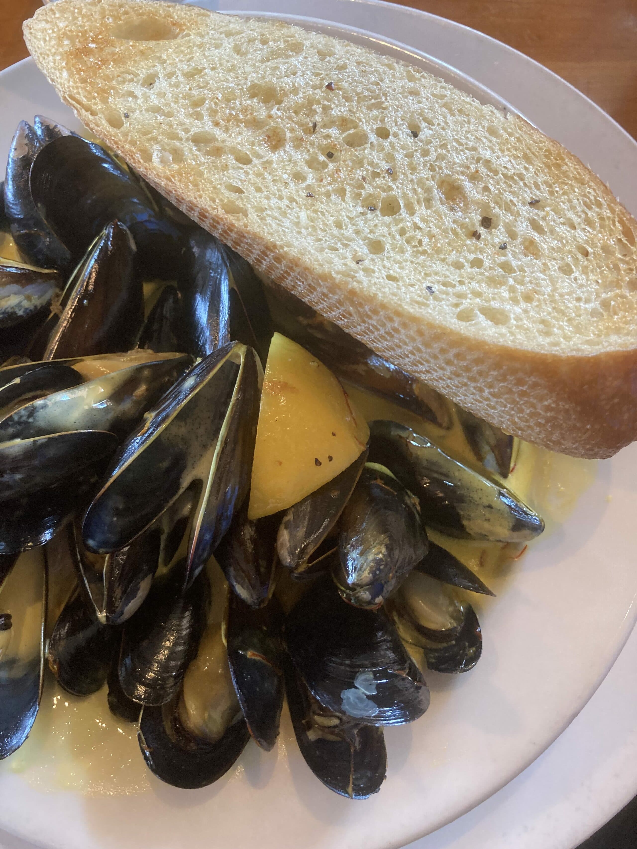 A plate of mussels served with a slice of bread.