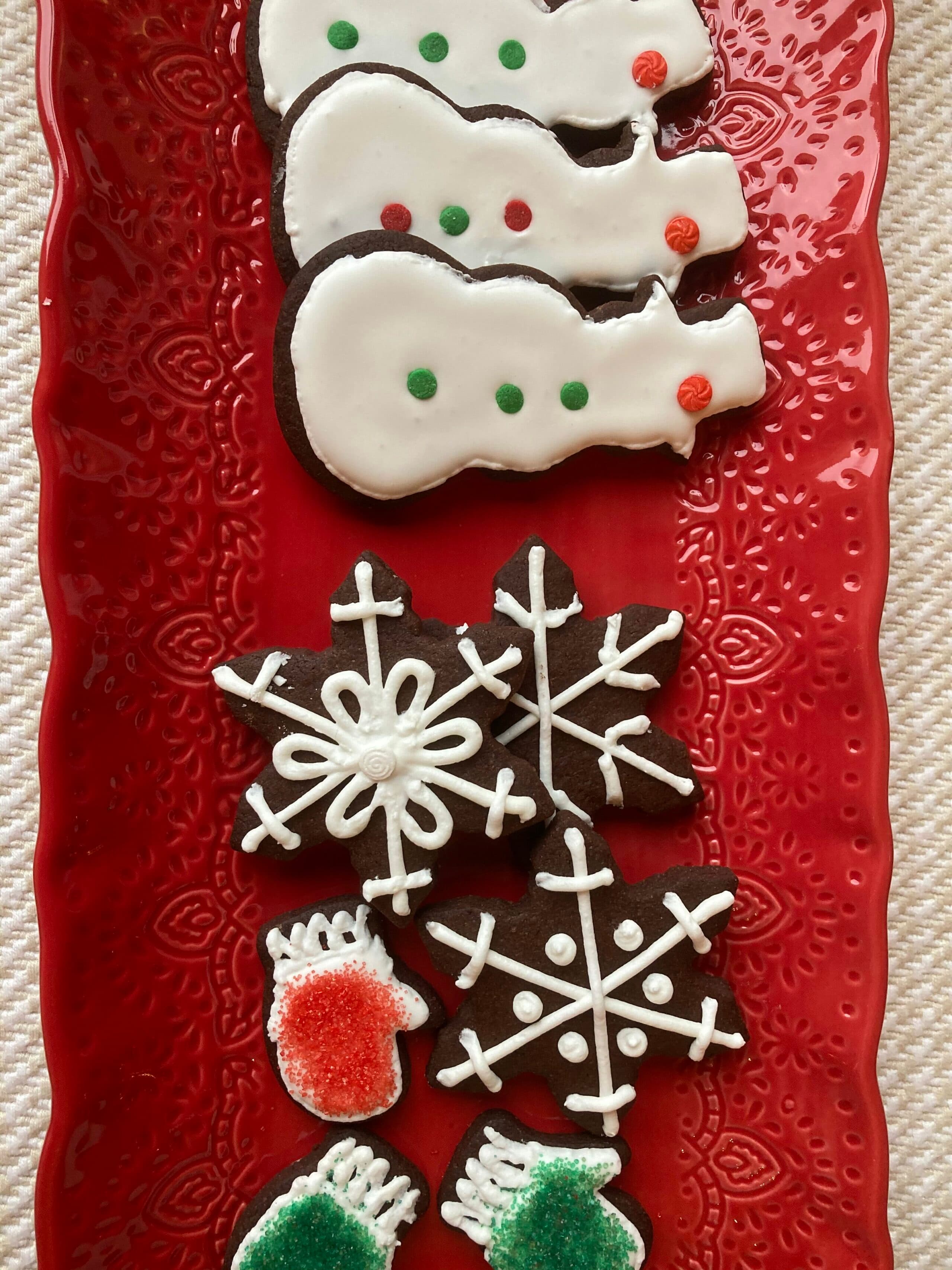 A festive red platter holds decorated cookies shaped like snowmen, snowflakes, and mittens.