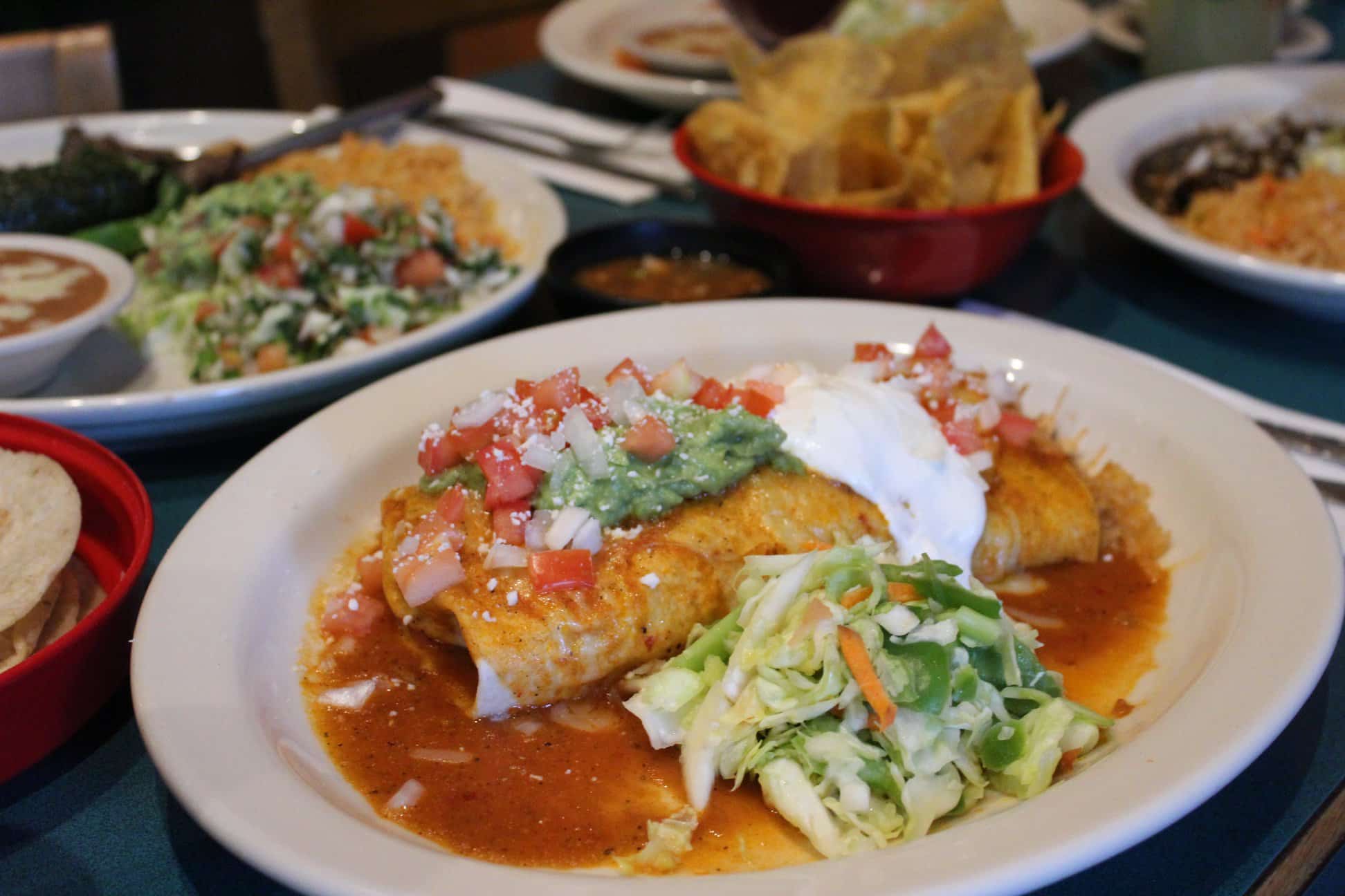 A plate of Mexican enchiladas topped with guacamole, tomatoes, sour cream, and served with a side of salad. A plate of Mexican enchiladas topped with guacamole, tomatoes, sour cream, and served with a side of salad.