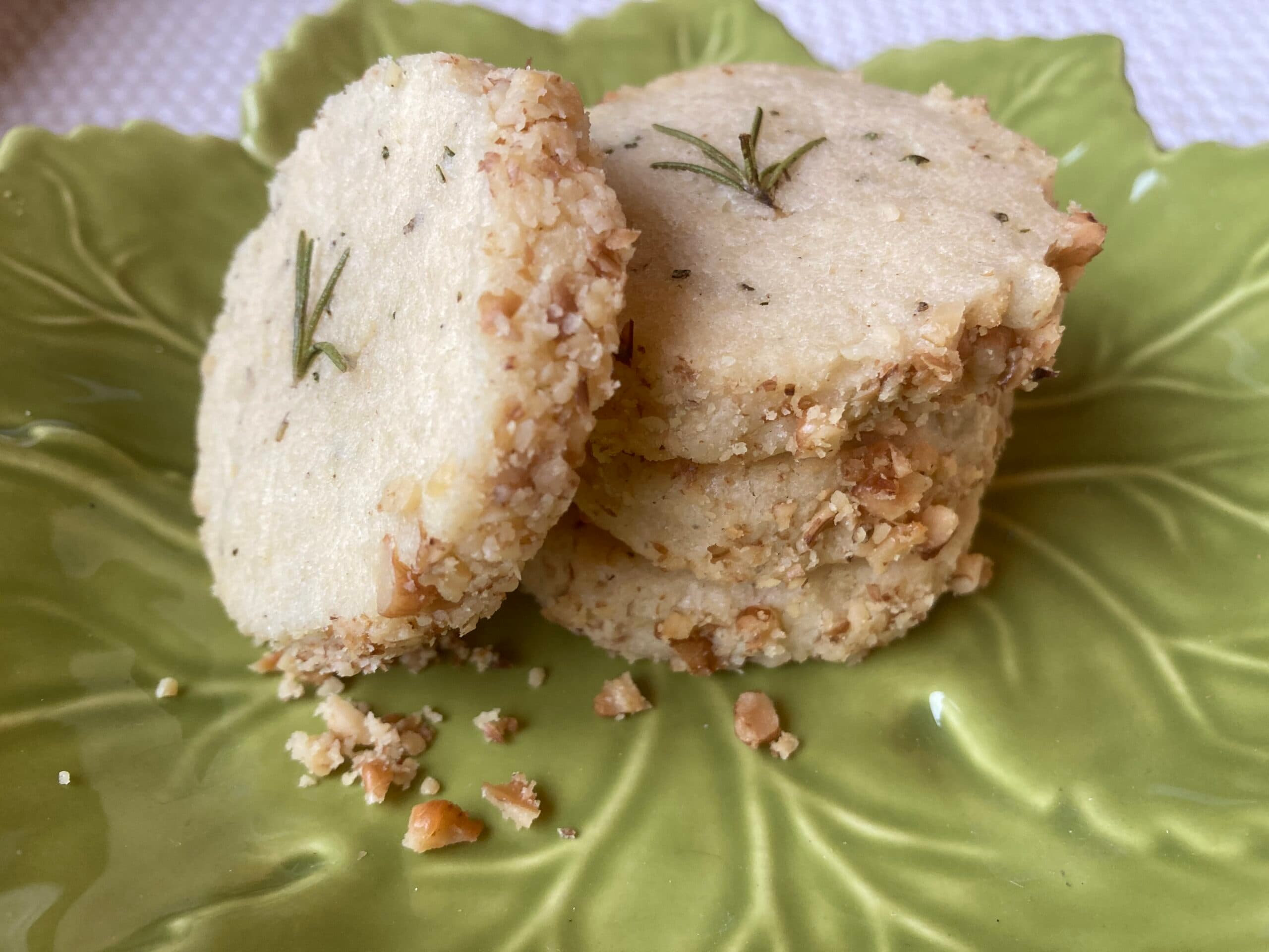 A stack of nut-coated, rosemary-infused cookies on a green leaf-shaped plate.