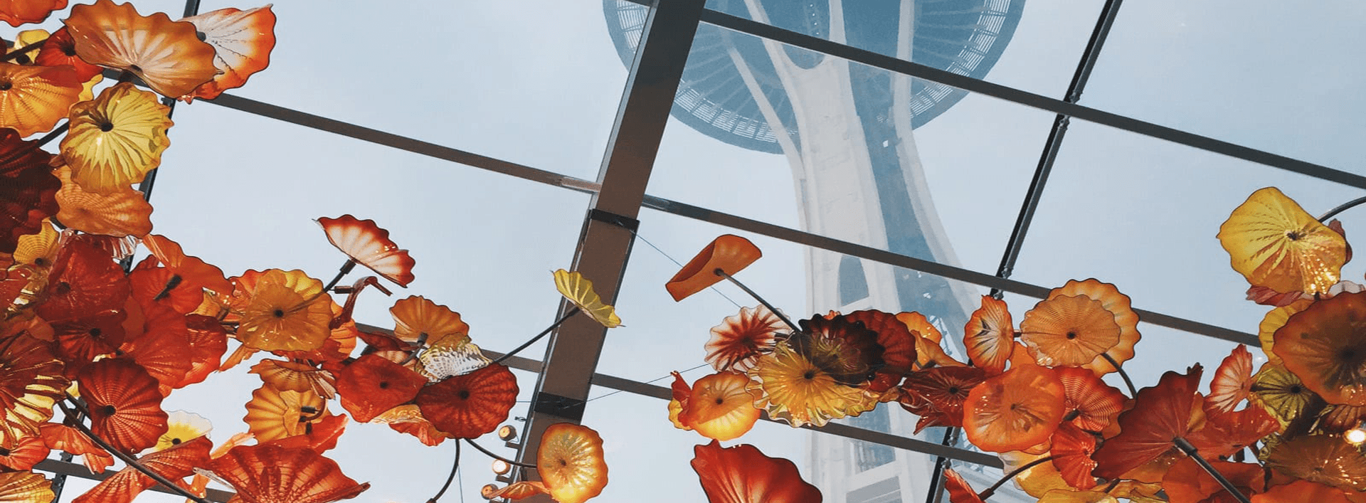Colorful glass flowers hang beneath a glass ceiling, framing a view of a tower above.