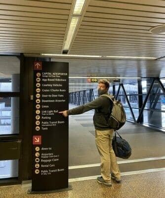 A man points to a signage board indicating transportation options at an airport terminal.