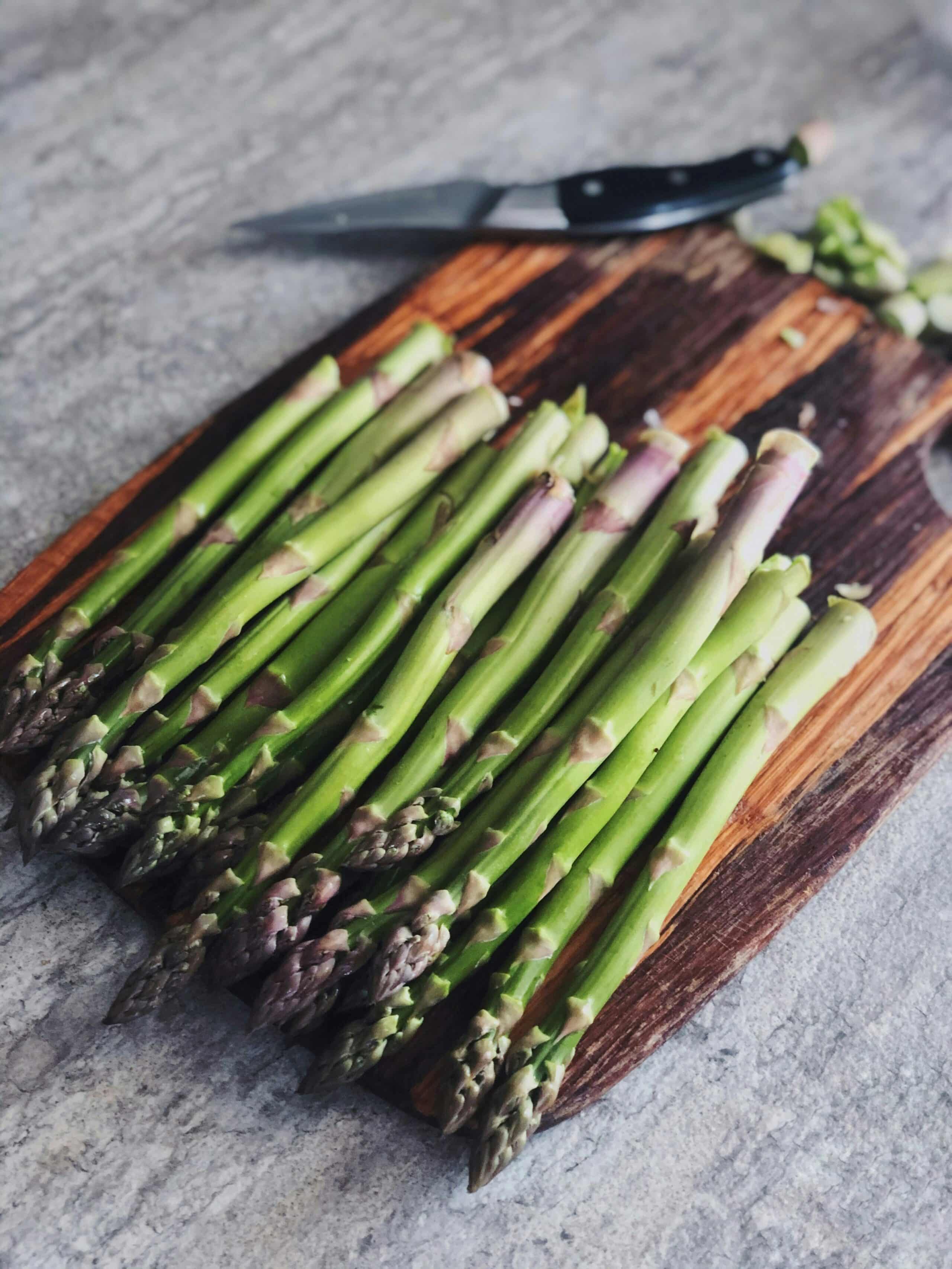 Fresh asparagus spears arranged on a wooden cutting board with a knife.