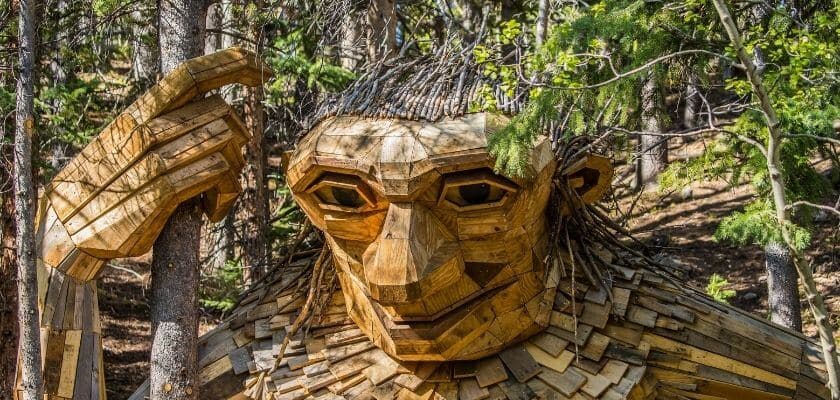 A large wooden troll sculpture stands among trees in a forest.