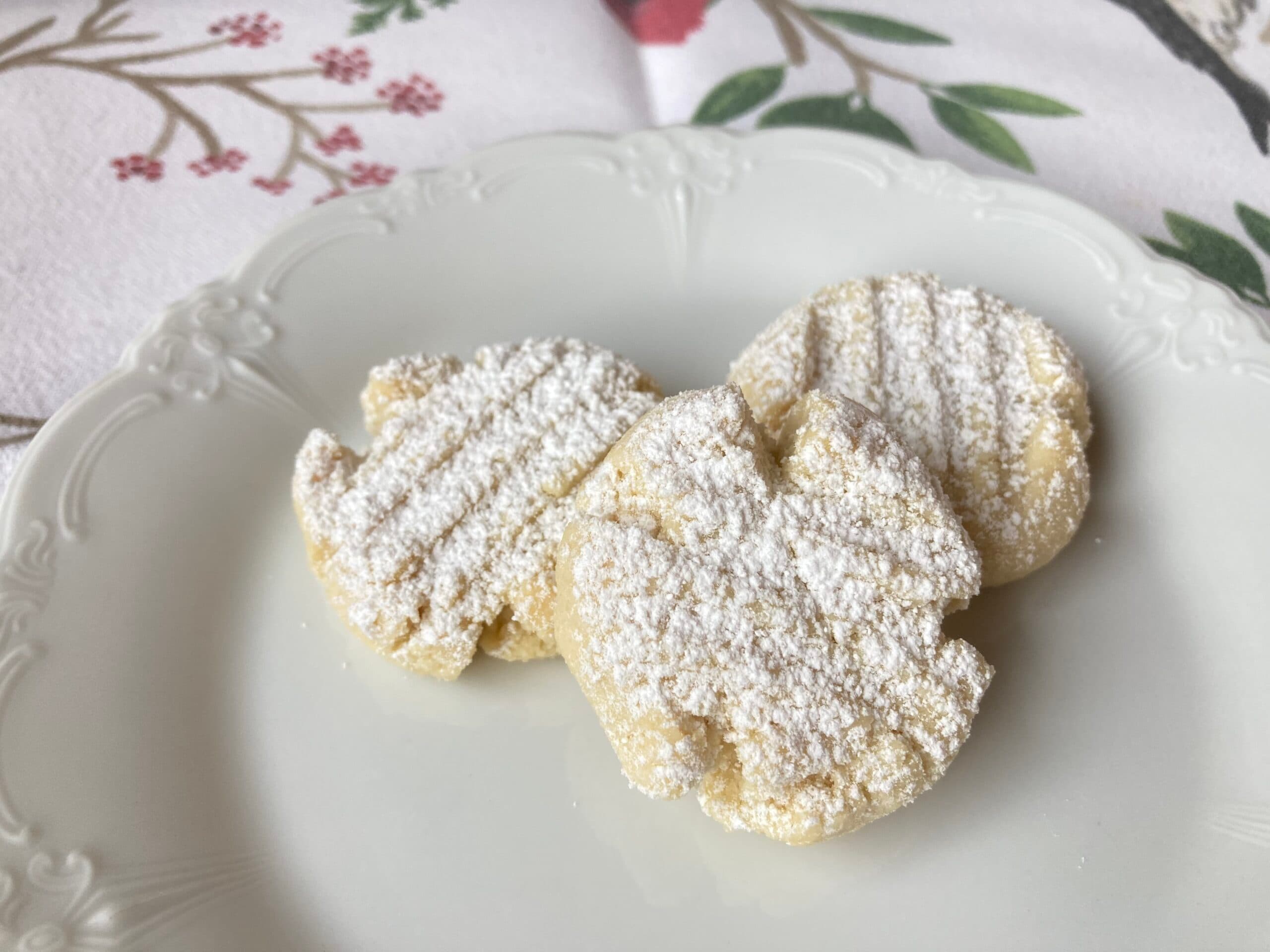 Three powdered sugar-coated cookies arranged on a decorative plate.