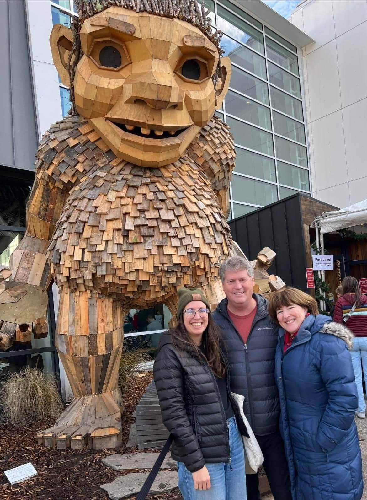 A wooden sculpture of a large troll stands behind three smiling people posing for a photo.