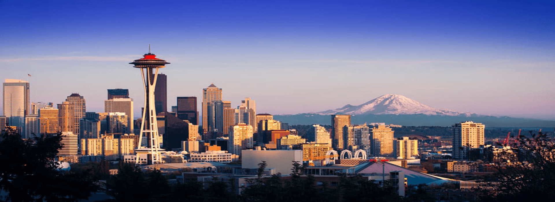 Seattle skyline at sunset with the Space Needle and Mount Rainier in the background.