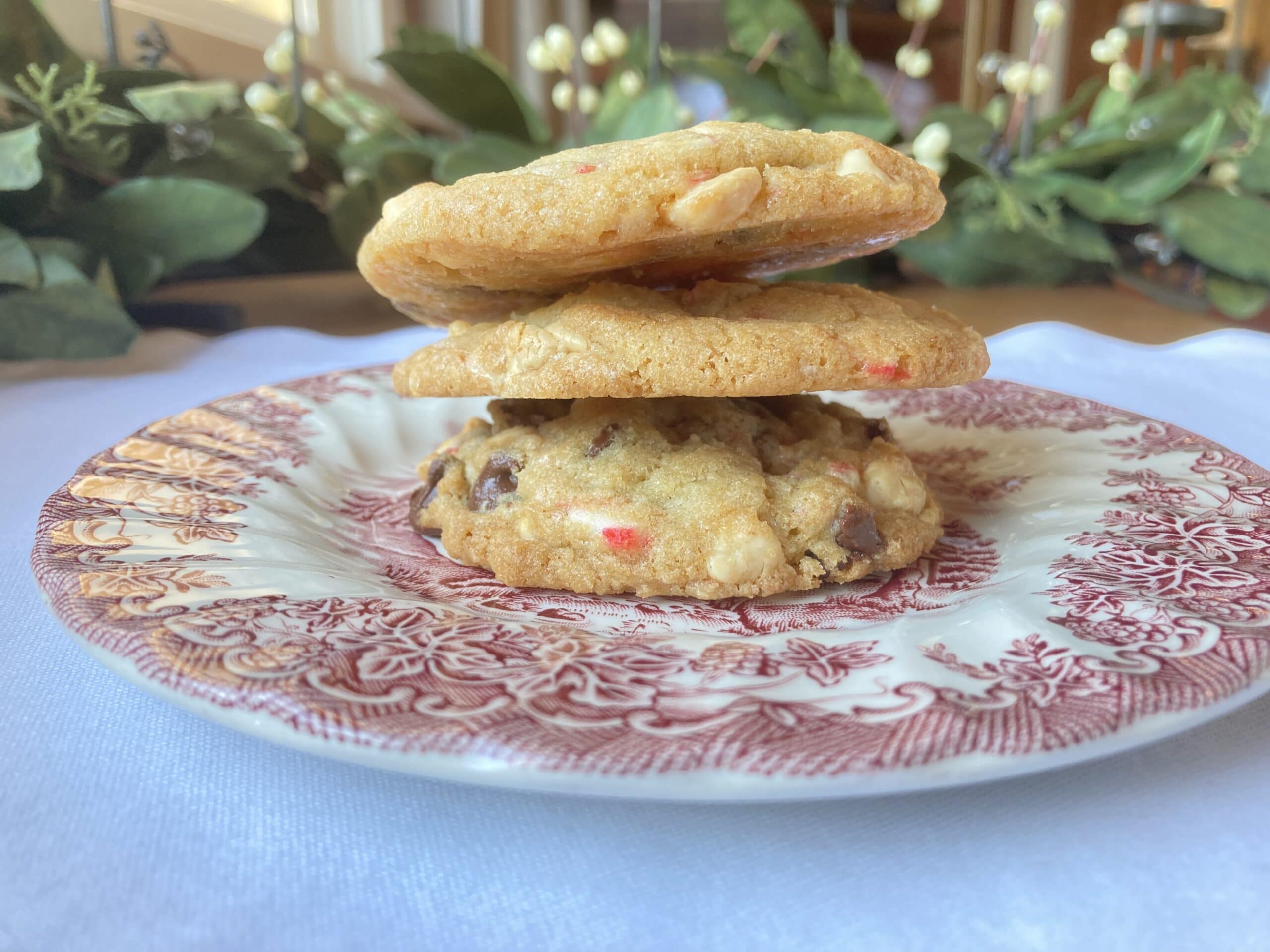 Three stacked cookies on a decorative plate, with a soft focus background of greenery.