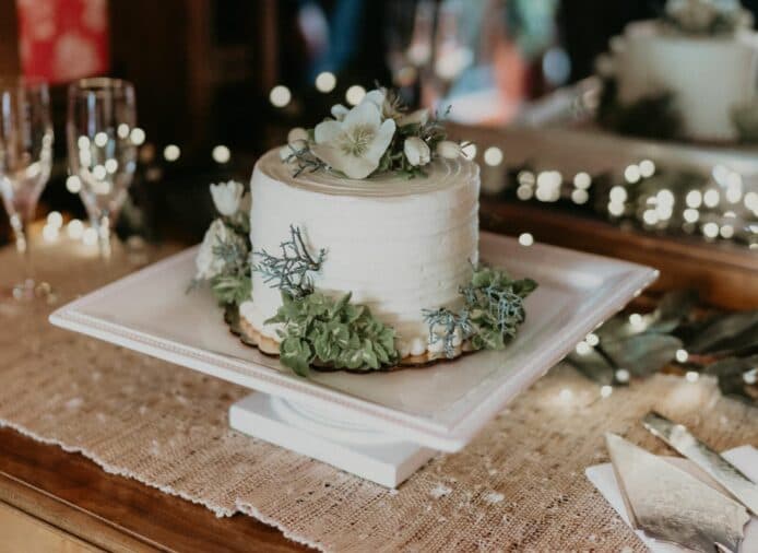 A beautifully decorated cake with floral accents on a white pedestal, surrounded by twinkling lights and elegant tableware.