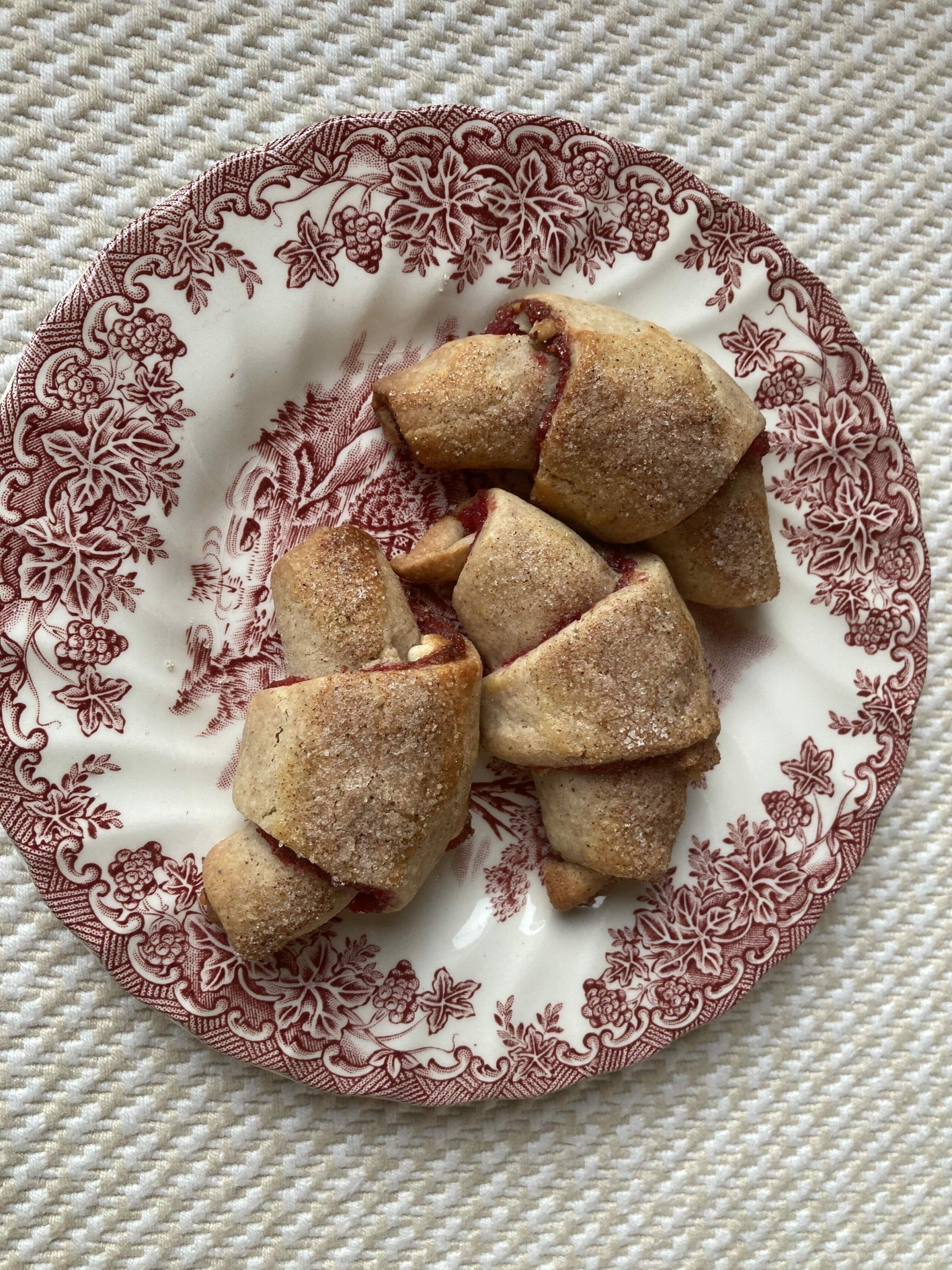A plate of freshly baked, sugar-dusted pastries filled with fruit on a decorative dish.