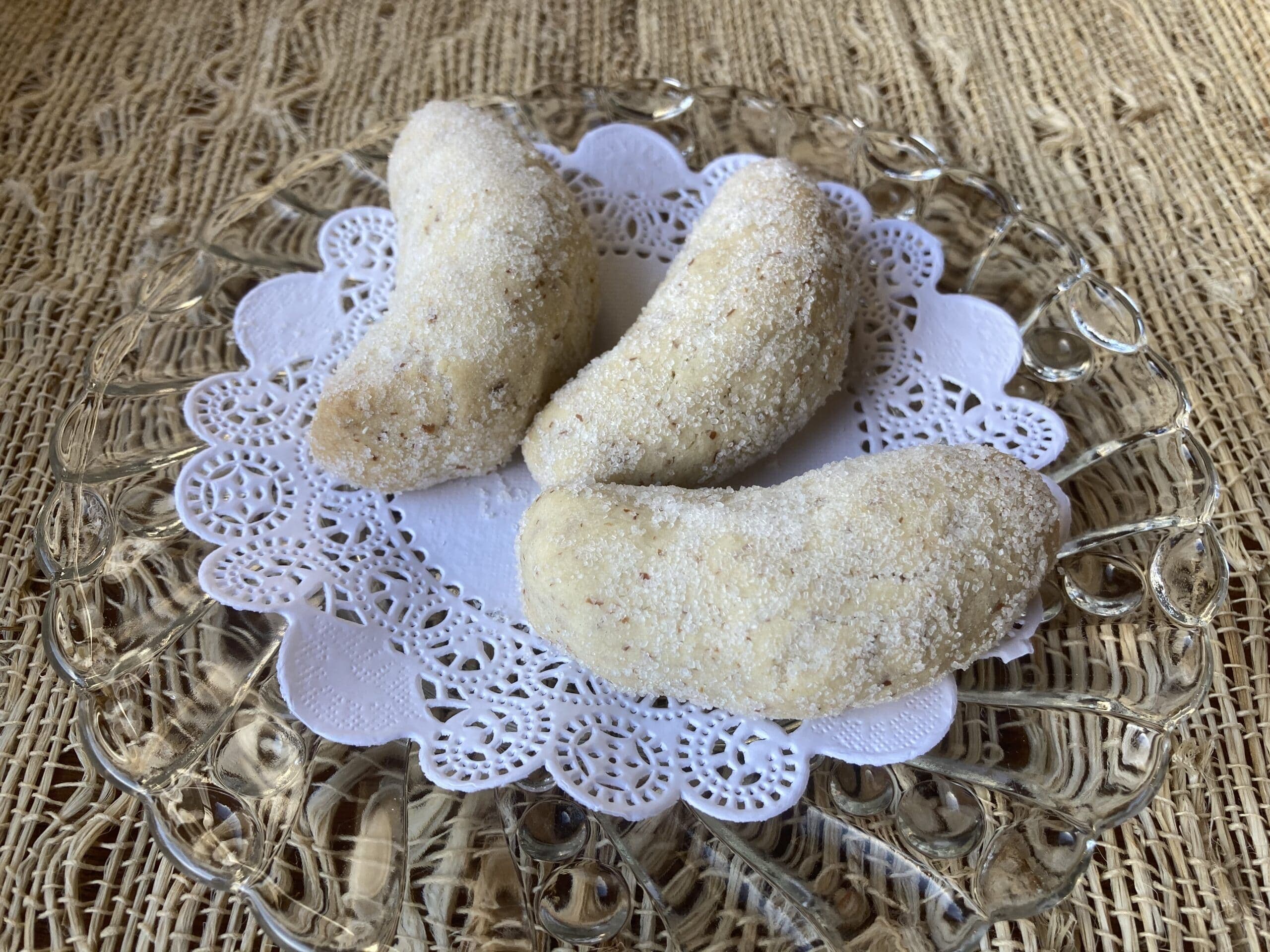 Three crescent-shaped sweets dusted with powdered sugar on a lace doily.