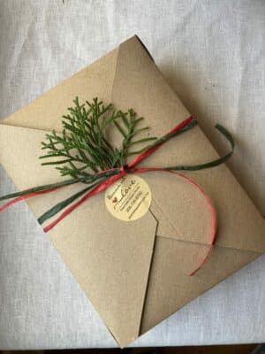 A beautifully wrapped gift in brown paper, adorned with greenery and a red and green ribbon.