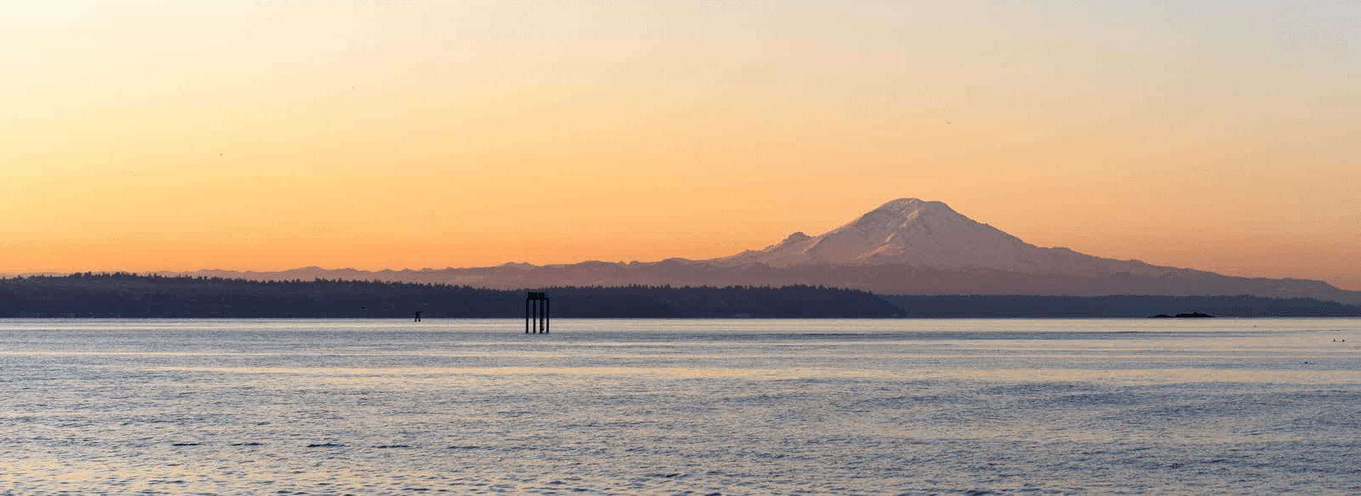 Sunset over a tranquil body of water with a snow-capped mountain in the background.