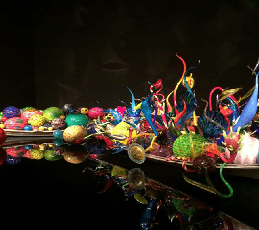 A vibrant, colorful glass sculpture arrangement reflecting in a dark space.