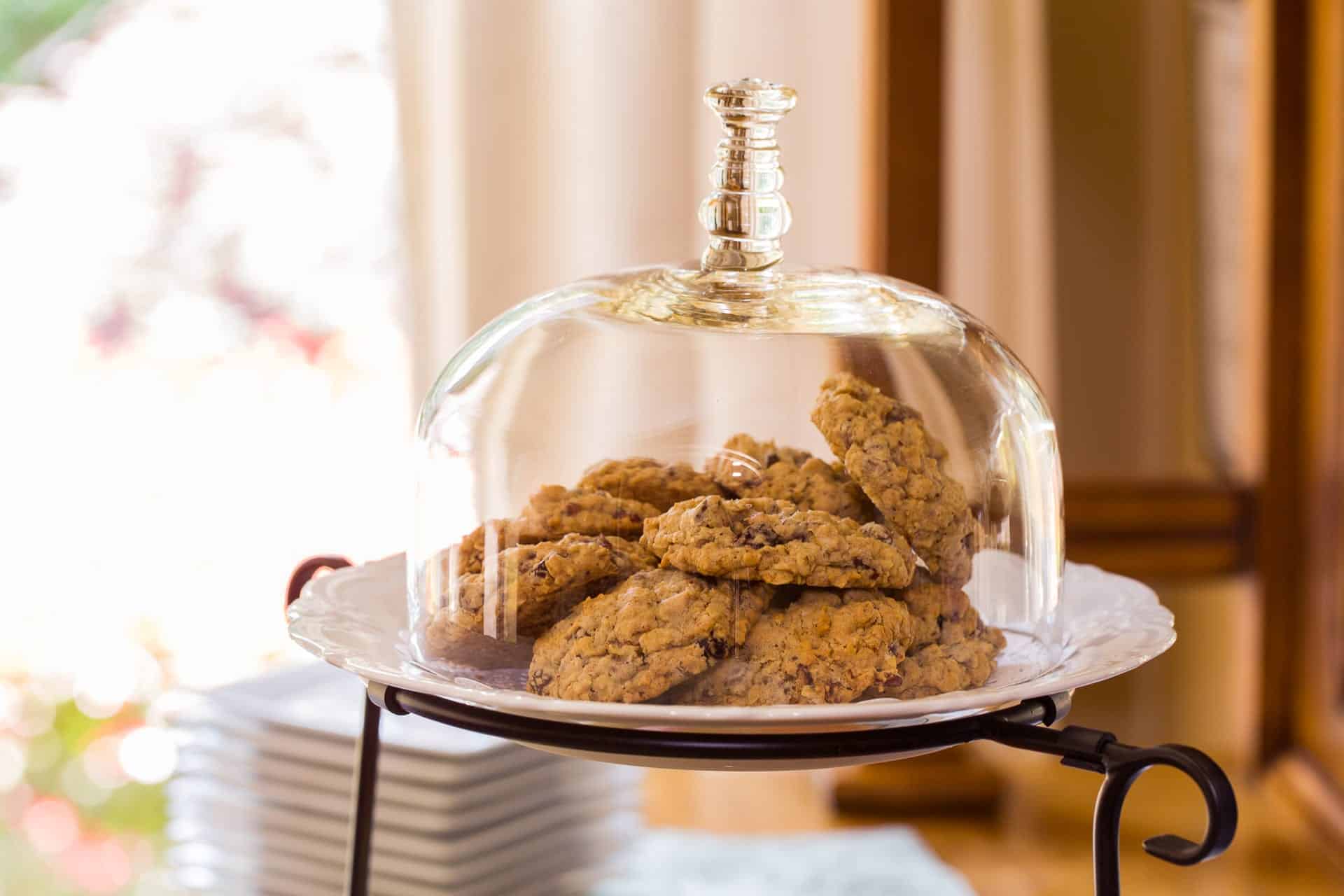 A glass cloche covers a plate of freshly baked cookies.